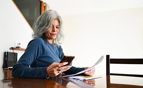 A lady using her smartphone in her home while looking over financials