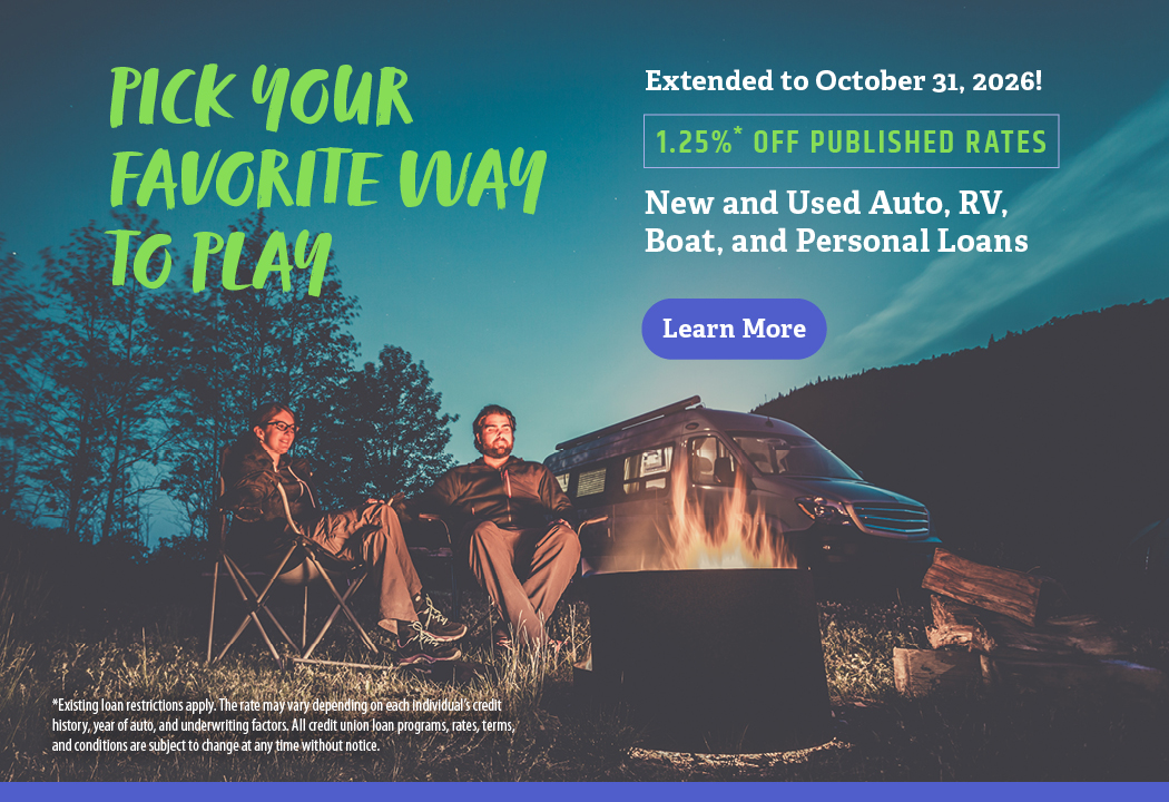 Man and woman sit around a campfire with a camper van behind them